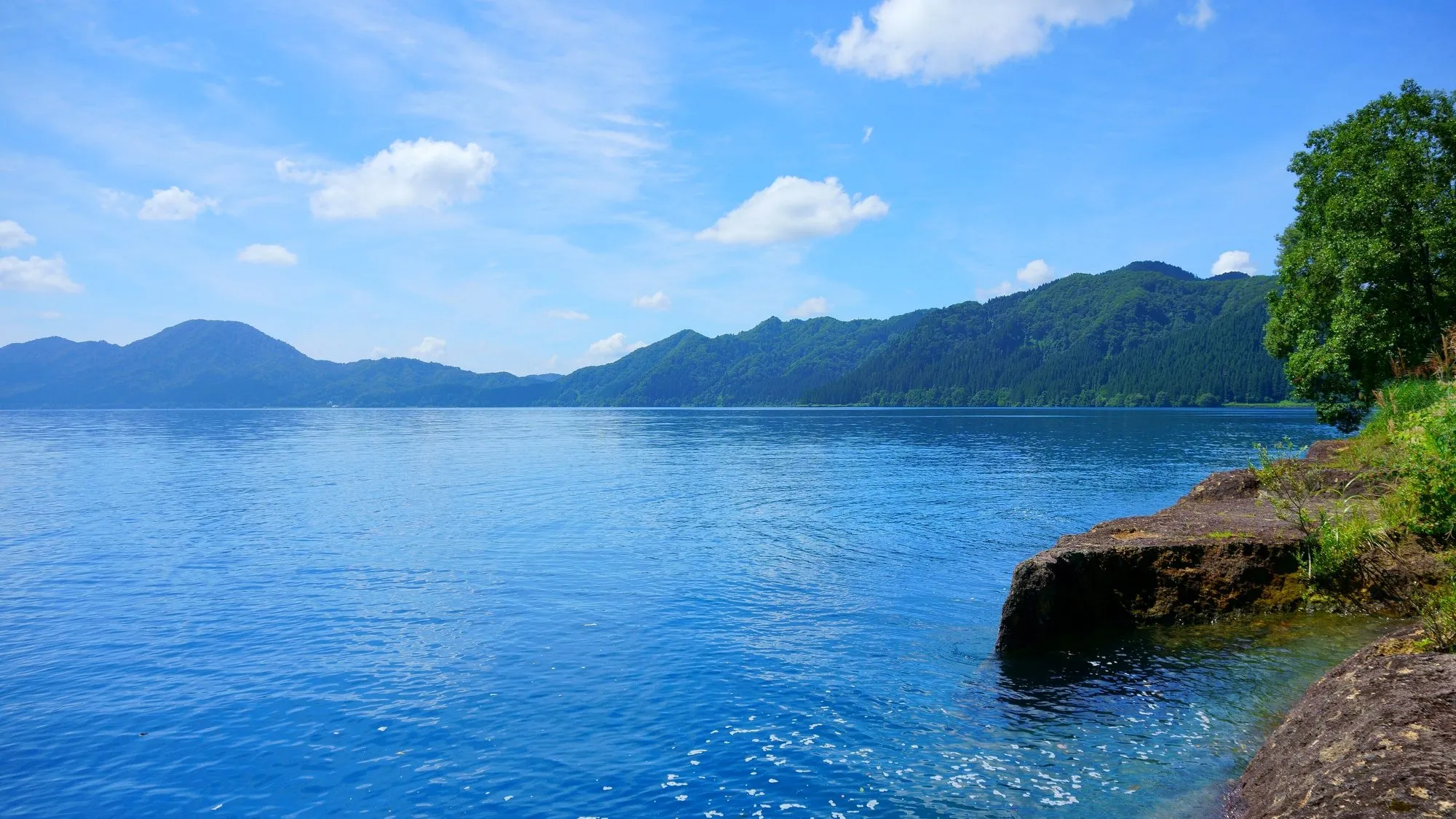御座石神社の近くから望む田沢湖。岸辺の浅瀬から一気に深い青へと落ち込む湖面